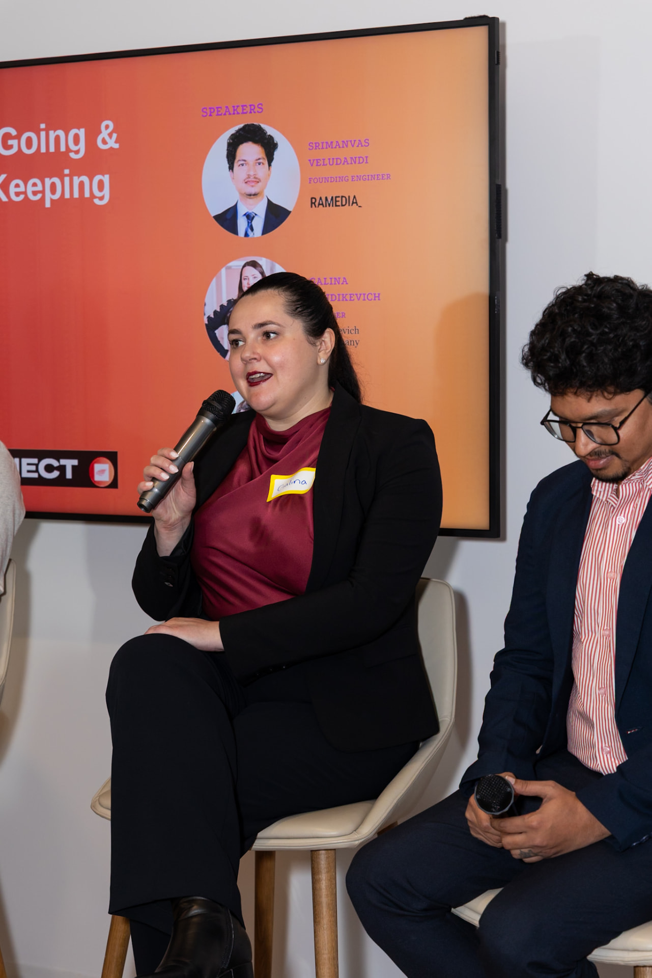 Three panelists seated on tall stools in front of a screen showing the panel title, with Galina Fendikevich speaking in the centre