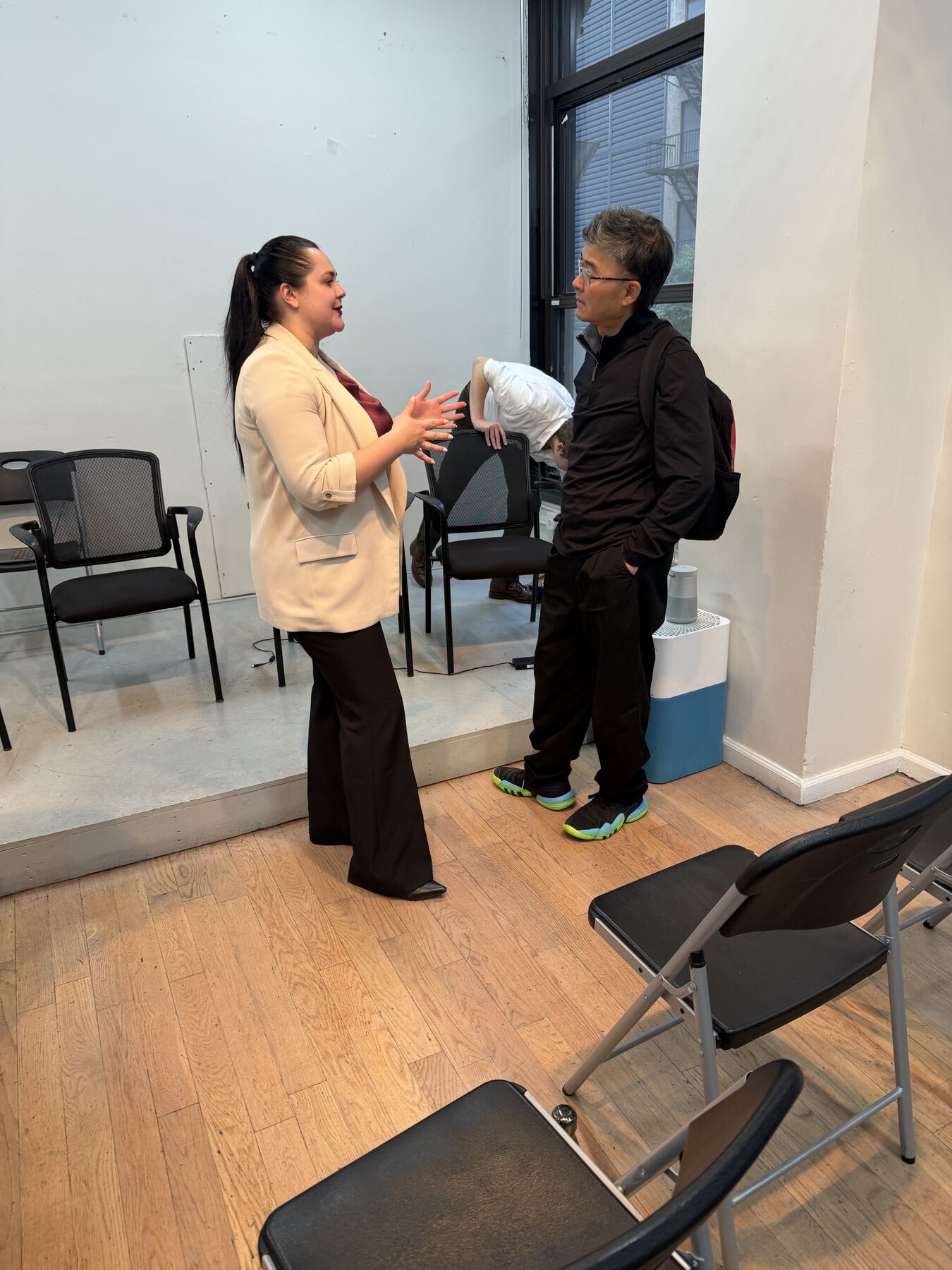 Galina Fendikevich talking with an attendee at AI Week New York, gesturing while wearing a cream blazer